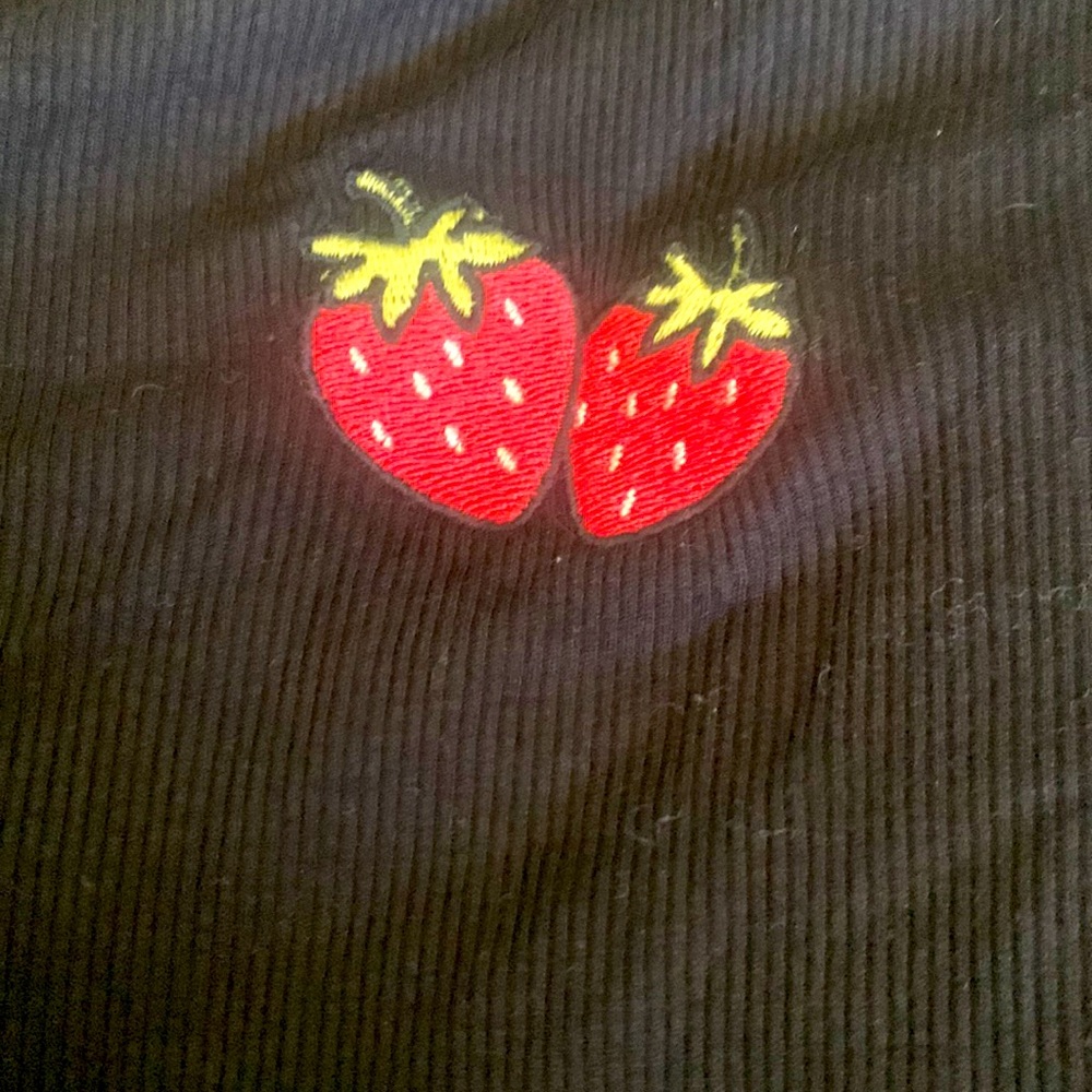 Black shirt ruffled in arm holes and bottom with 2 strawberry’s in the middle